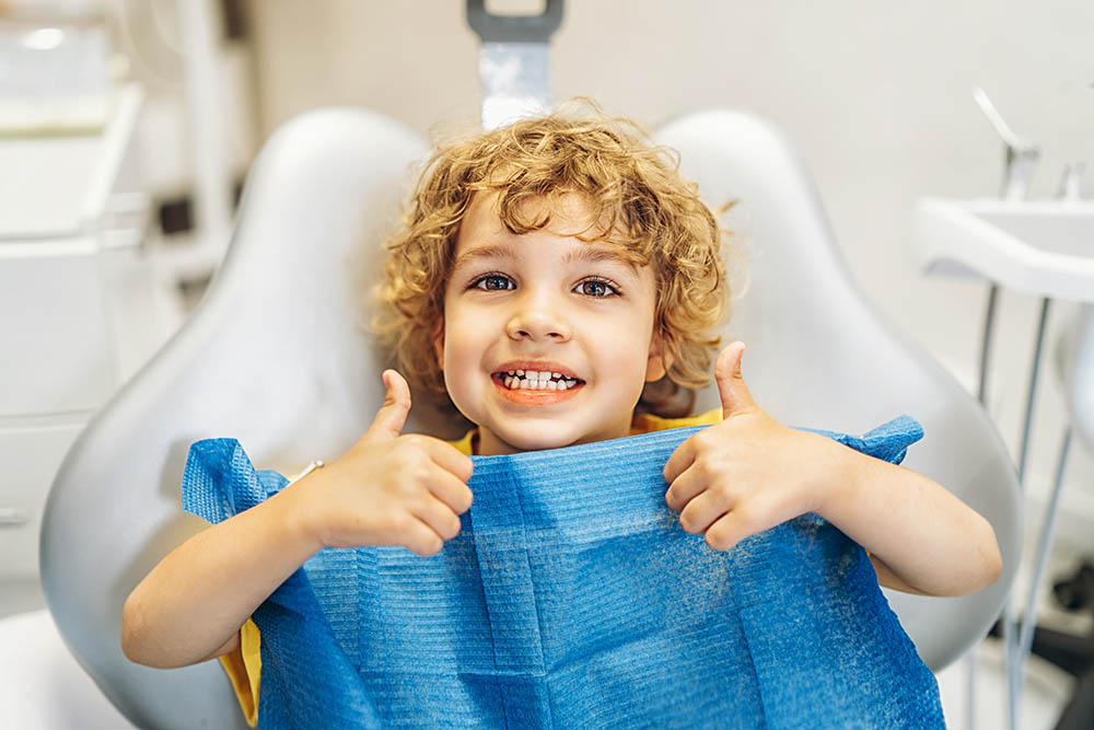 Happy cute little boy in dental ofiice showing thumbs up after treatment