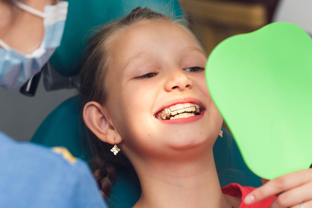 The girl looks at the braces on her teeth in the mirror